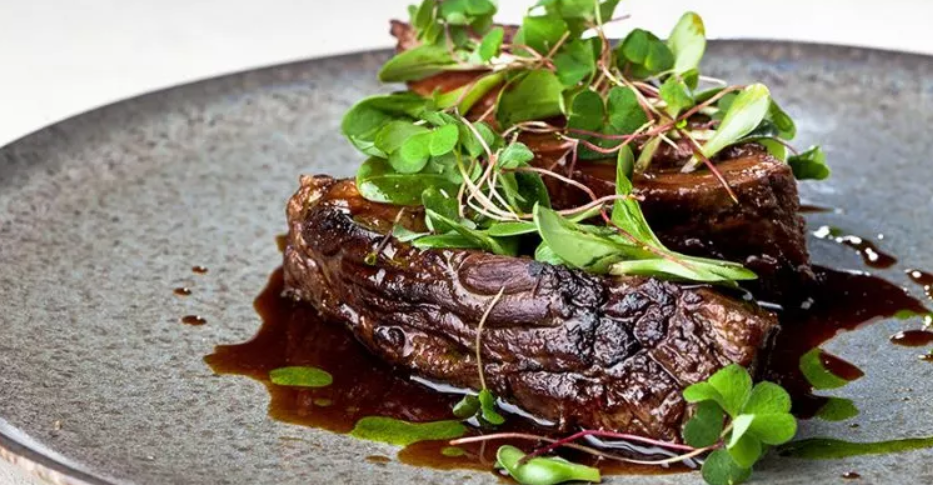 Angerichtetes Hauptgericht mit Fleisch, Sauce und frischen Kräutern