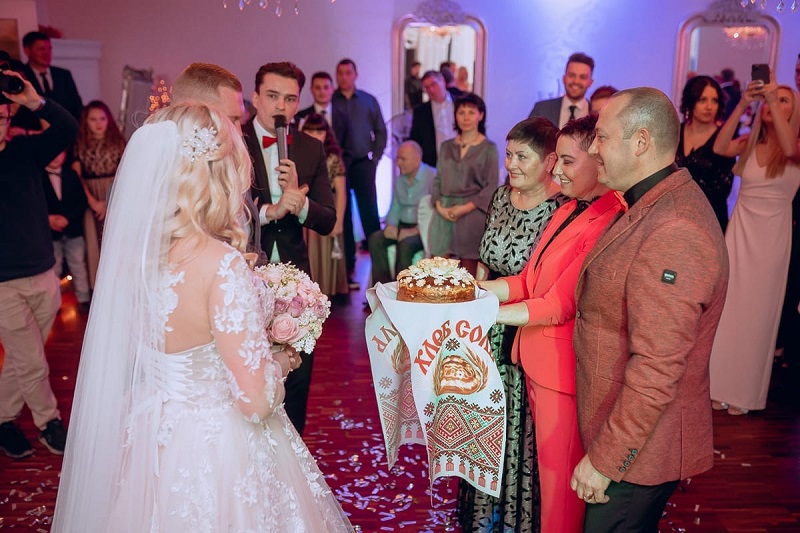 Tamada Alex und die Eltern empfangen das Brautpaar bei der russische Hochzeit mit dem Brot und Salz