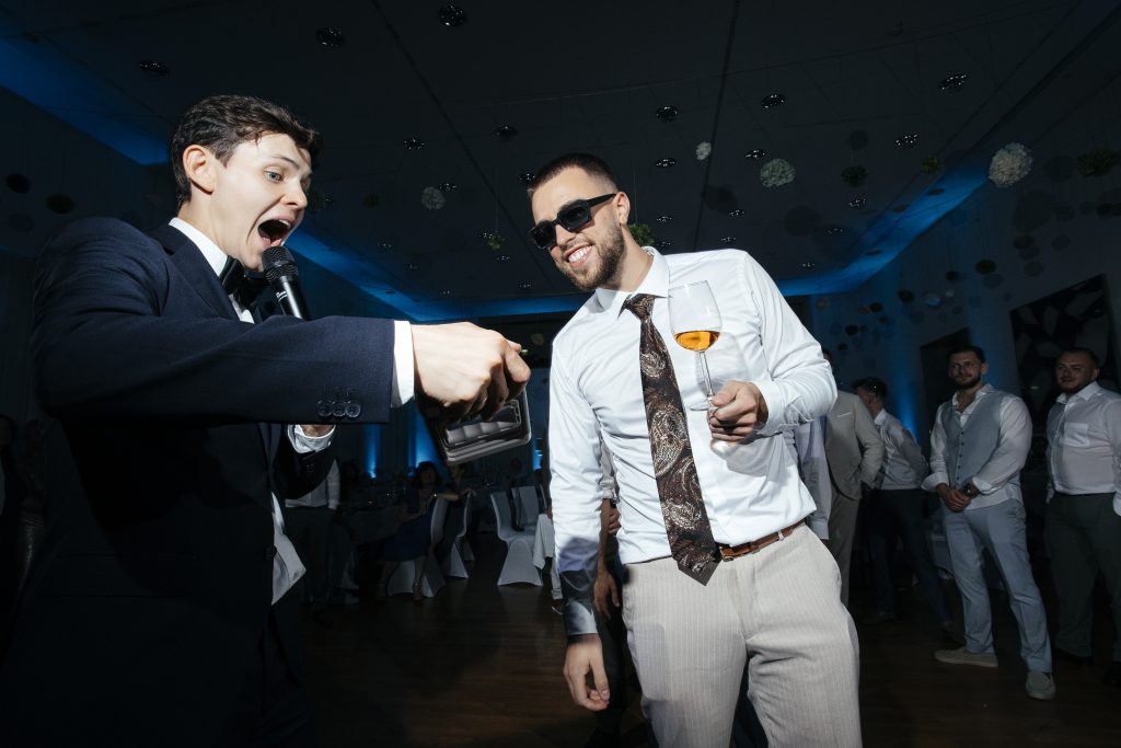 Tamada Alex Lux mit Mikrofon und einem lachenden Gast auf der Hochzeit