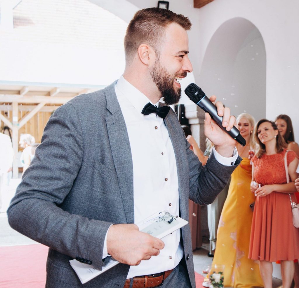 Chris moderiert mit Mikrofon vor den Gästen