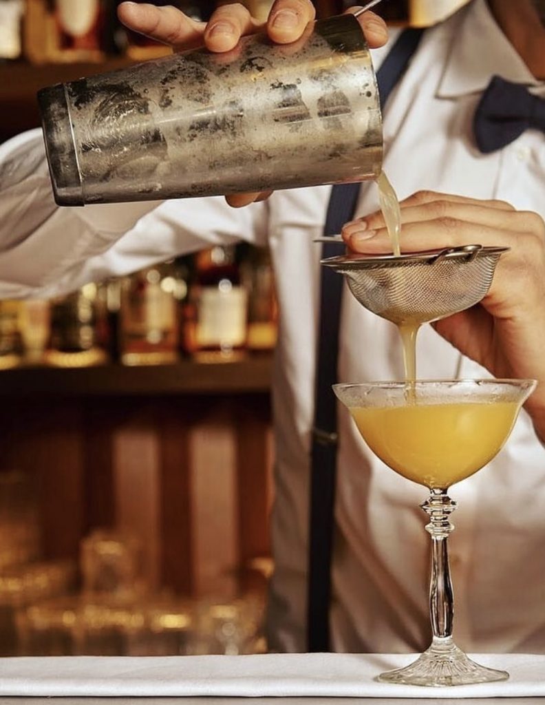 Cocktail wird durch ein Barsieb in eine Schale eingeschenkt