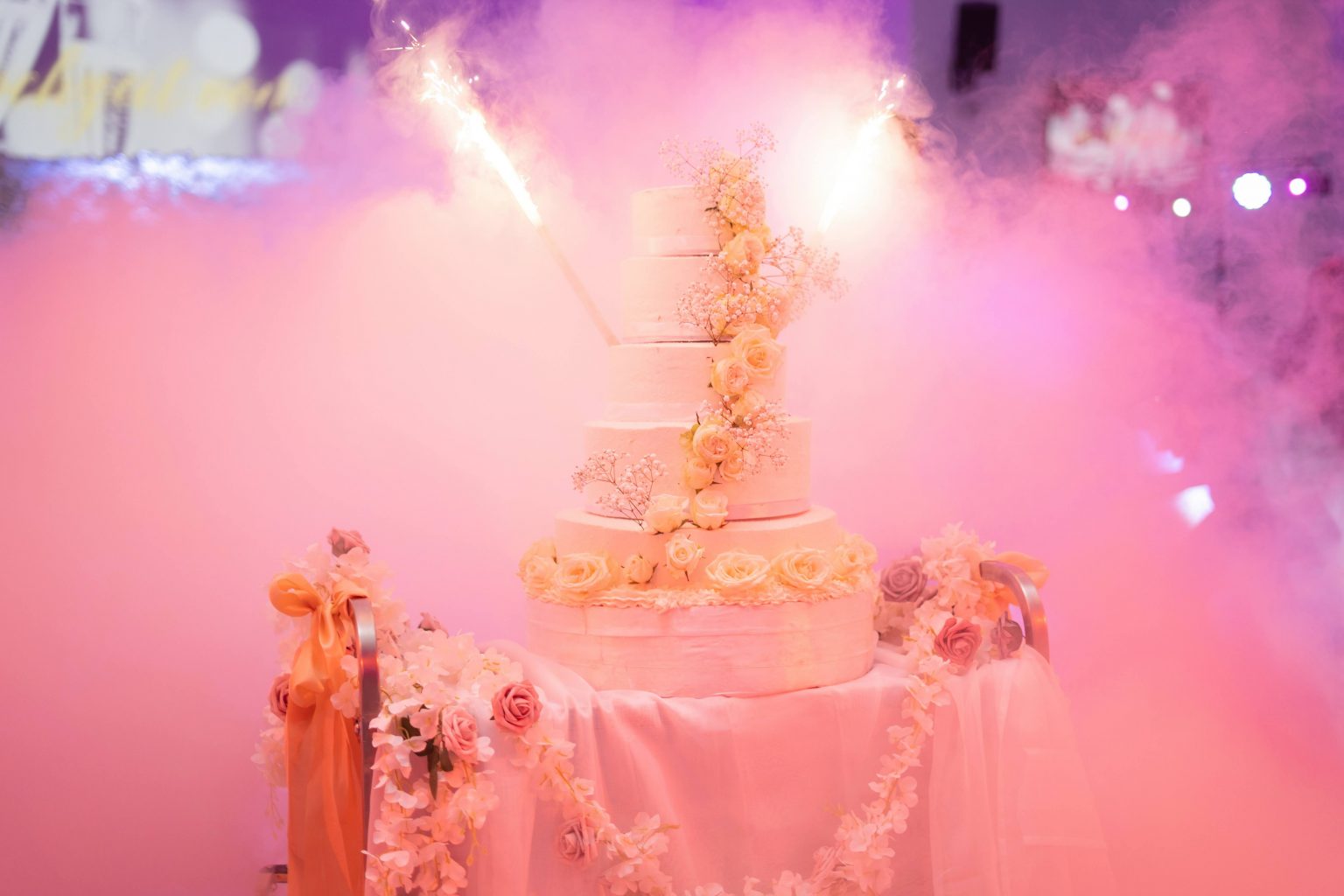 Mehrstöckige Hochzeitstorte mit Blumenschmuck und rosafarbenen Lichteffekten