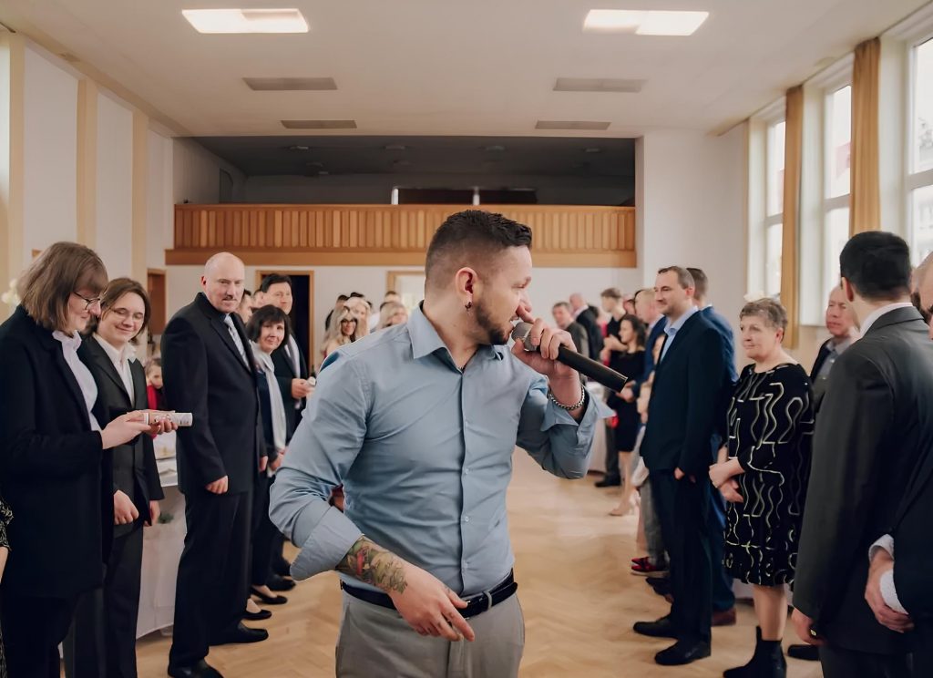 Stas moderiert mit Mikrofon zwischen den Hochzeitsgästen im Saal