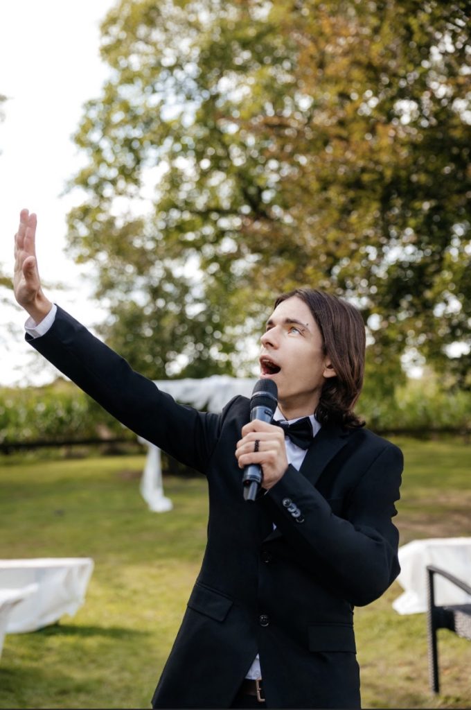 Joker mit Mikrofon und ausgestreckter Hand im Freien