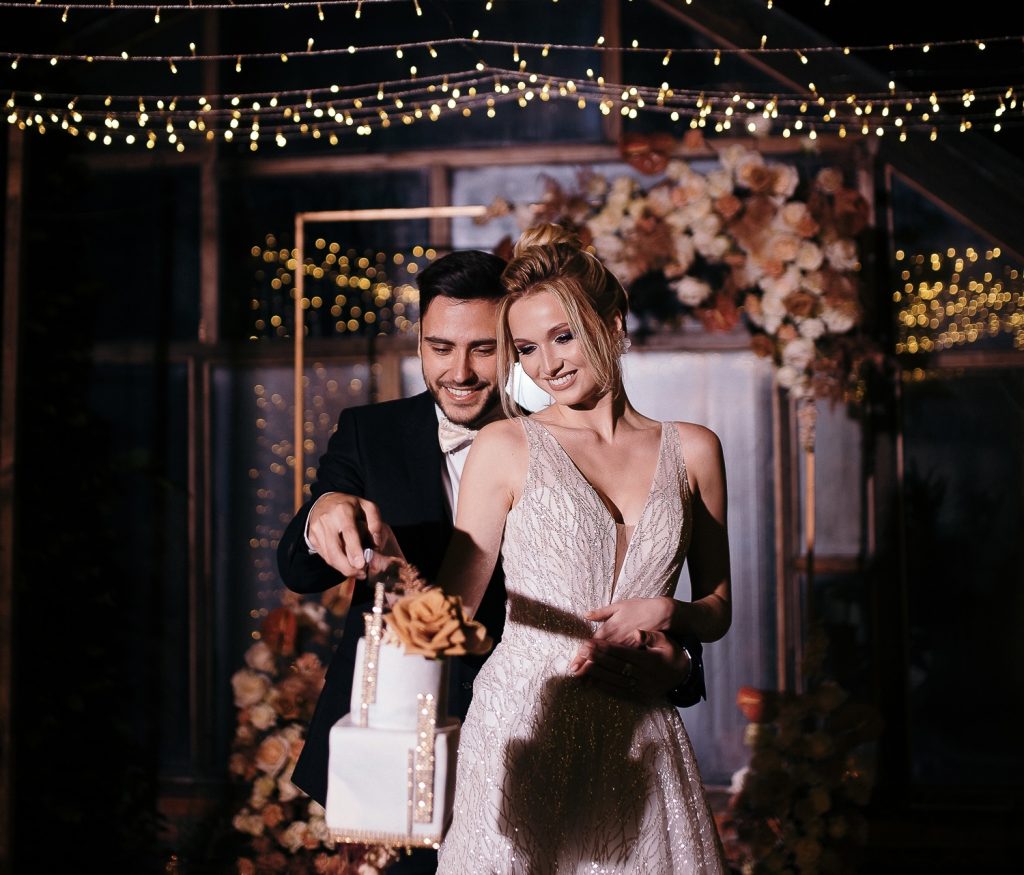 Brautpaar schneidet gemeinsam die Hochzeitstorte unter Lichterketten an