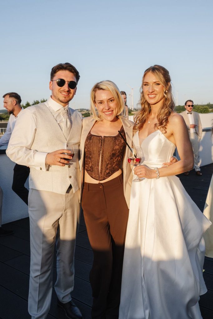 Hochzeitsmoderatorin Lera steht mit dem Brautpaar auf einer Terrasse in der Abendsonne