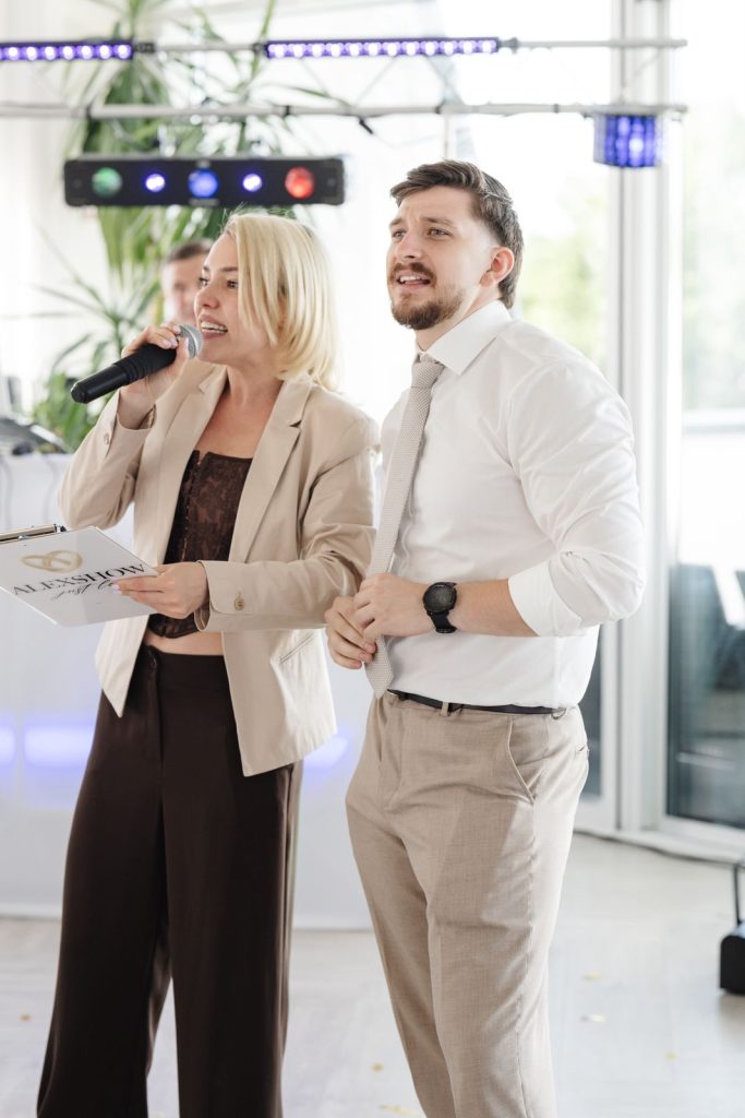 Hochzeitsmoderatorin Lera moderiert mit Mikrofon und AlexShow-Mappe neben einem Hochzeitsgast