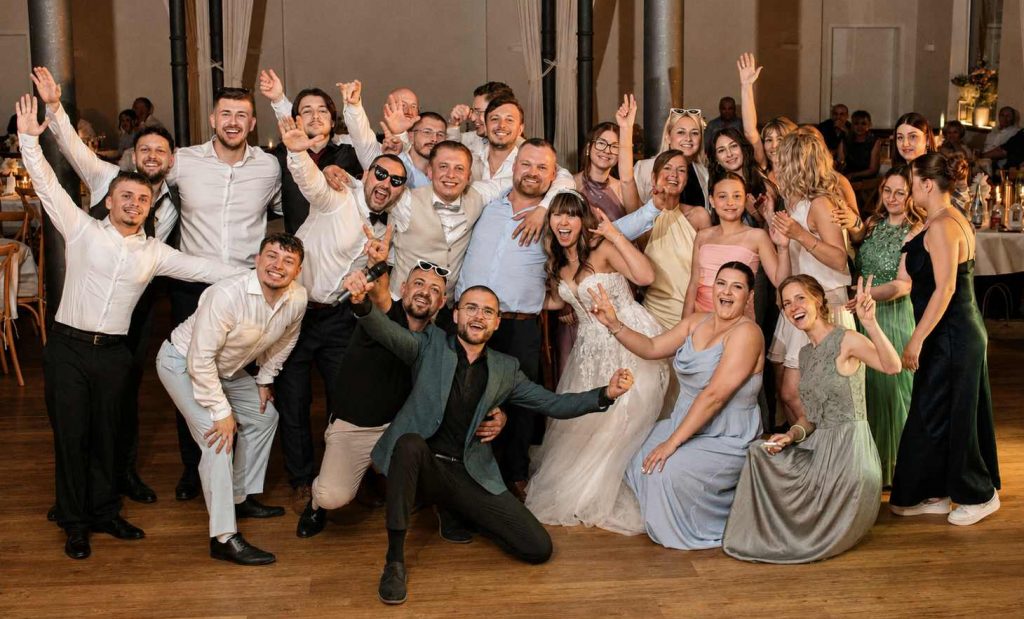 Brautpaar und Hochzeitsgäste feiern ausgelassen mit Hochzeitsmoderator Davis auf der Tanzfläche