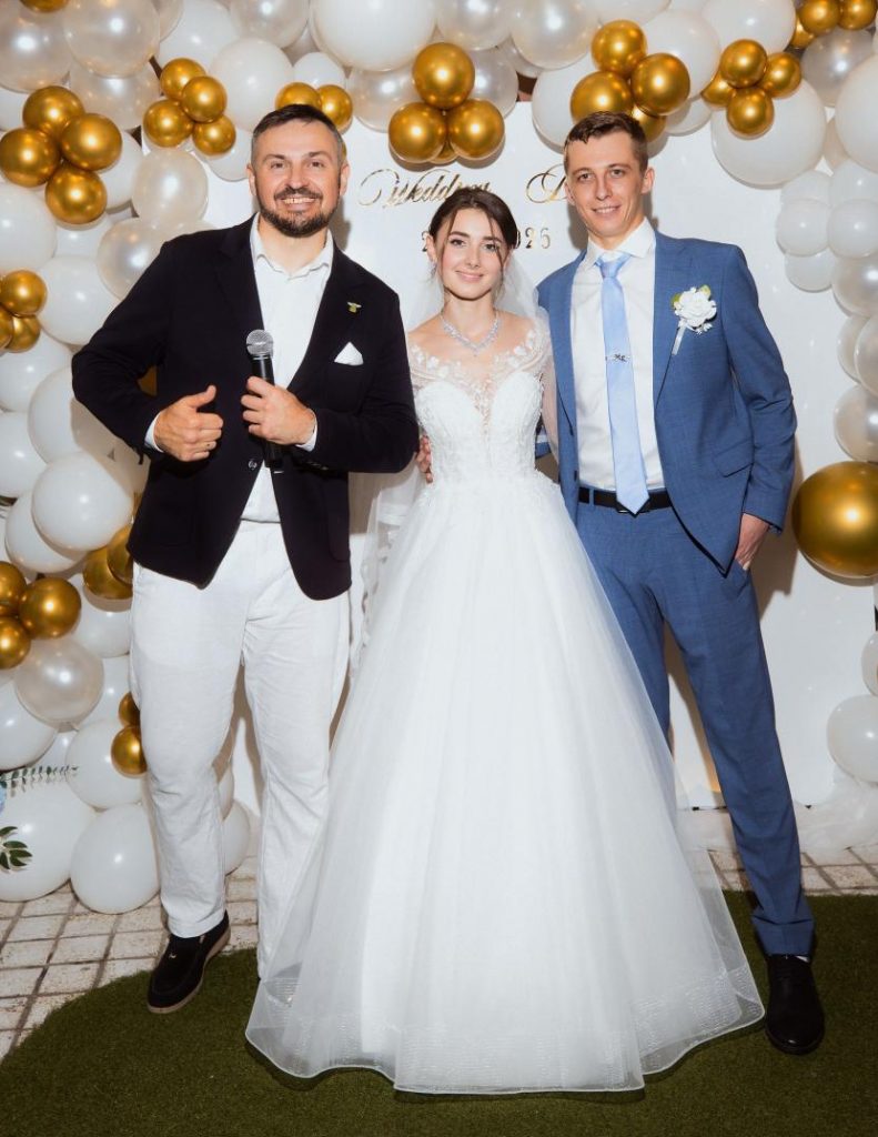 Serge mit einem Brautpaar vor einer festlichen Fotowand