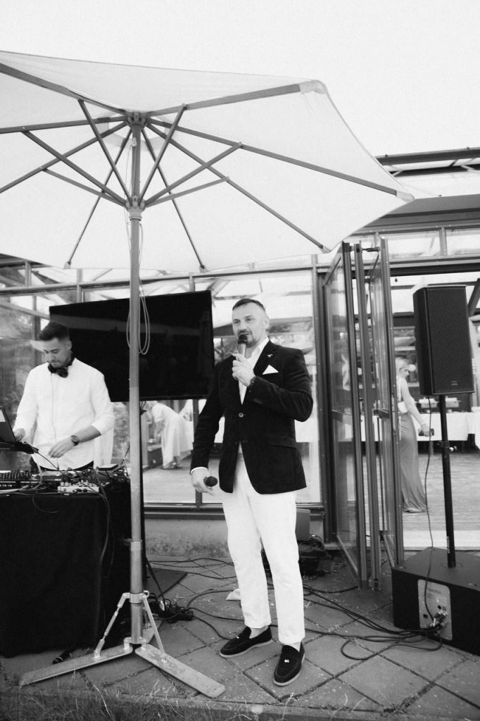 Serge mit Mikrofon neben dem DJ-Pult bei einer Hochzeitsfeier