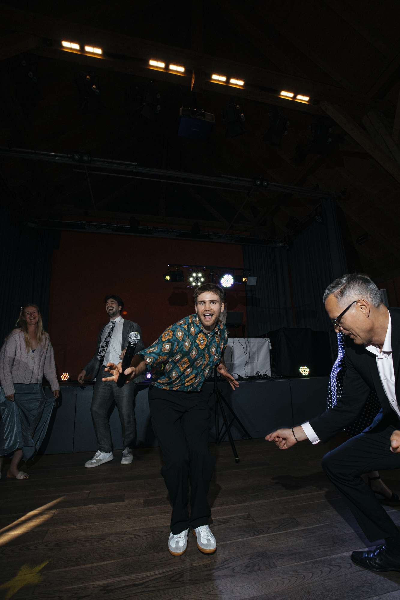 Moderator in gemustertem Hemd tanzt mit lachenden Gästen auf der Tanzfläche