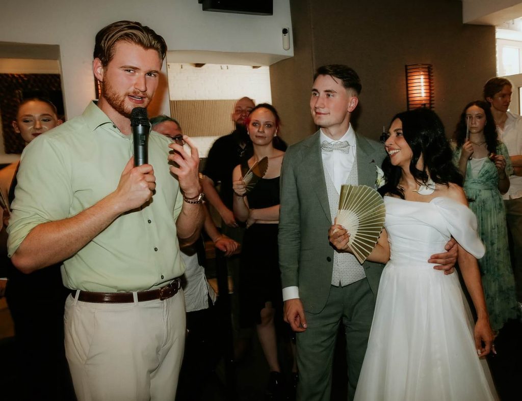 Hochzeitsmoderator Sanja aus Dortmund moderiert mit Mikrofon die Hochzeitsfeier neben dem Brautpaar