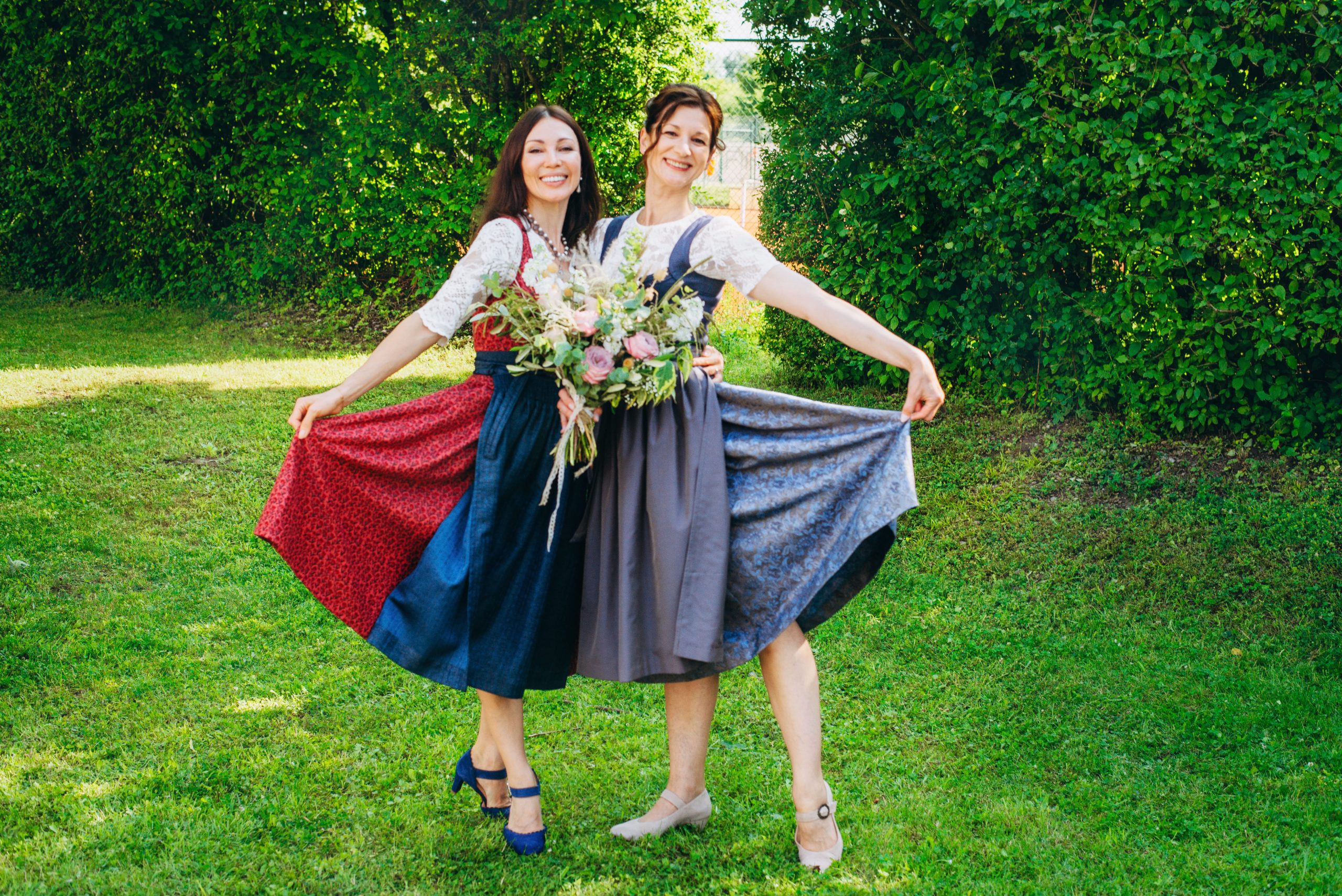 Braut und Trauzeugin in Dirndl mit Blumenstrauß im Grünen – bayerische Hochzeit