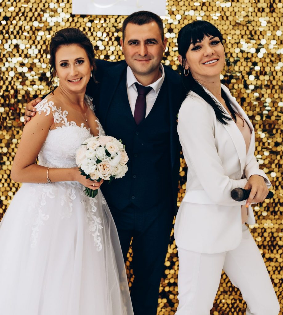 Elena mit einem Brautpaar vor einer goldenen Fotowand
