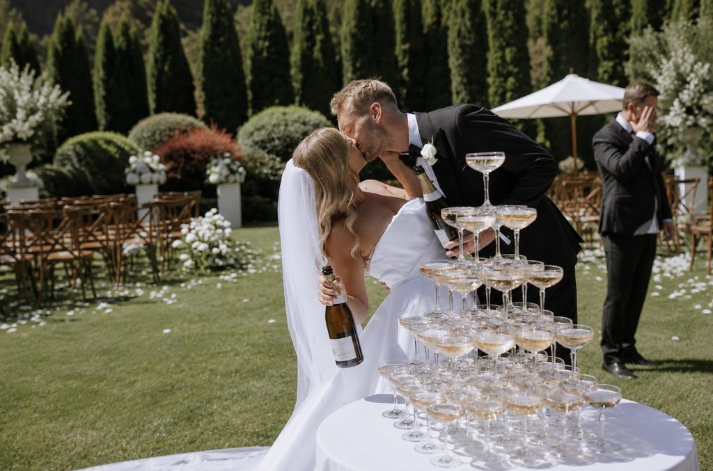 Brautpaar küsst sich vor einer Sektempyramide auf einer eleganten Hochzeit.
