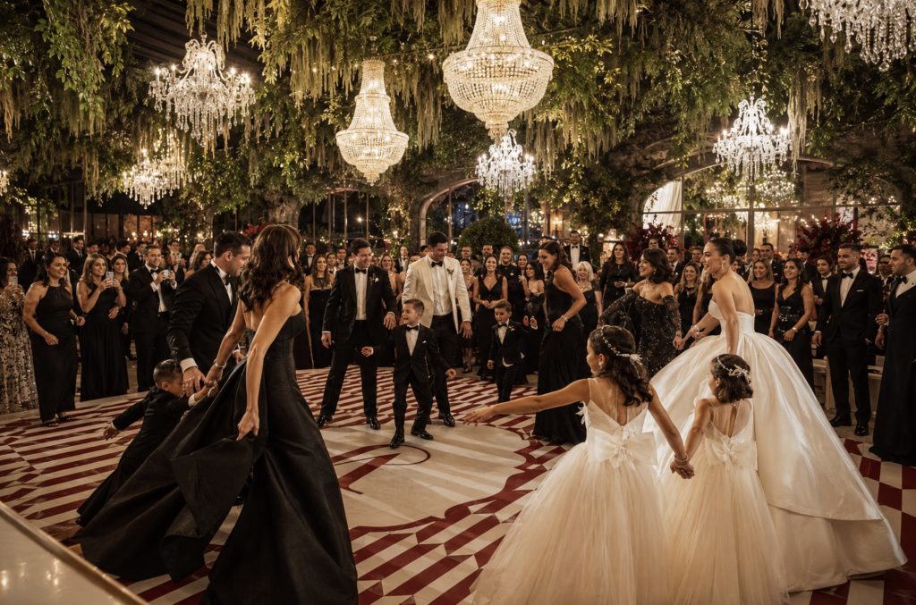 Gäste feiern gemeinsam mit dem Brautpaar auf einer luxuriösen Hochzeit in Italien unter funkelnden Kronleuchtern.