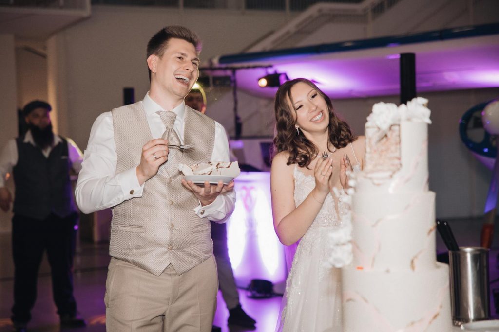 Lachendes Brautpaar neben der mehrstöckigen Hochzeitstorte während der Feier