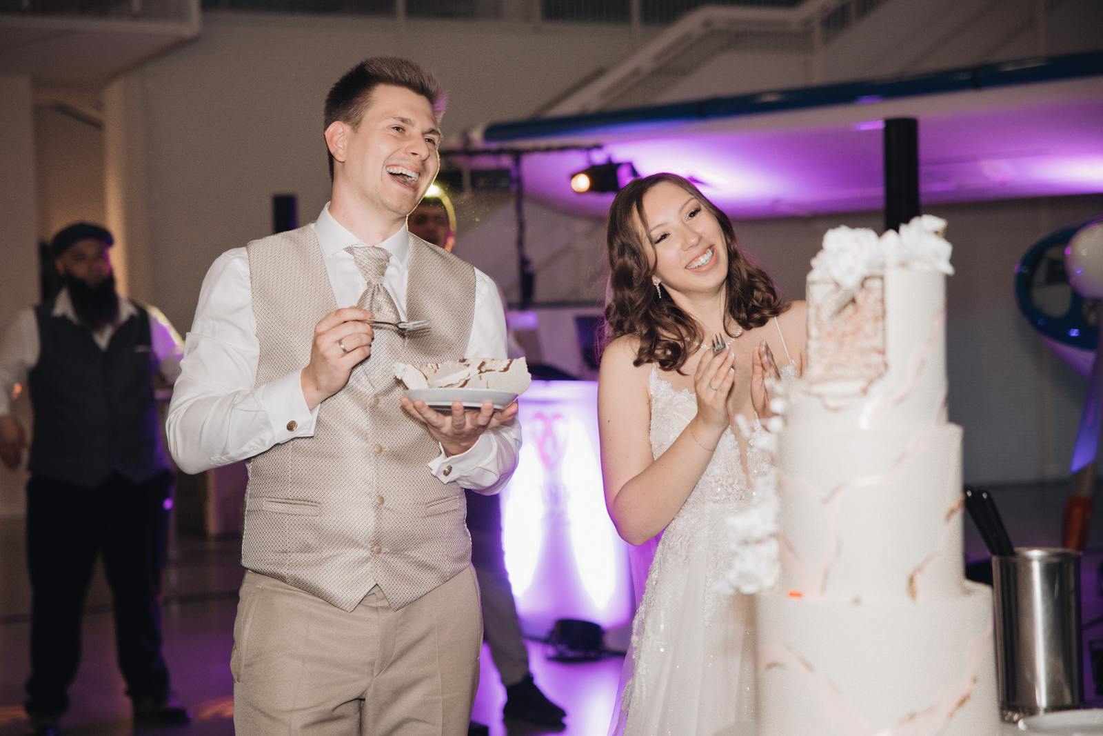 Violetta und Denis lachen neben ihrer mehrstöckigen Hochzeitstorte.