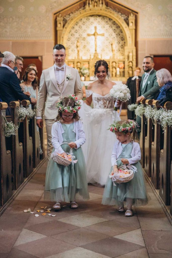 Ineinander gelegte Hände des Brautpaares neben dem weißen Brautstrauß während der Trauung bei einer Hochzeit in Köln