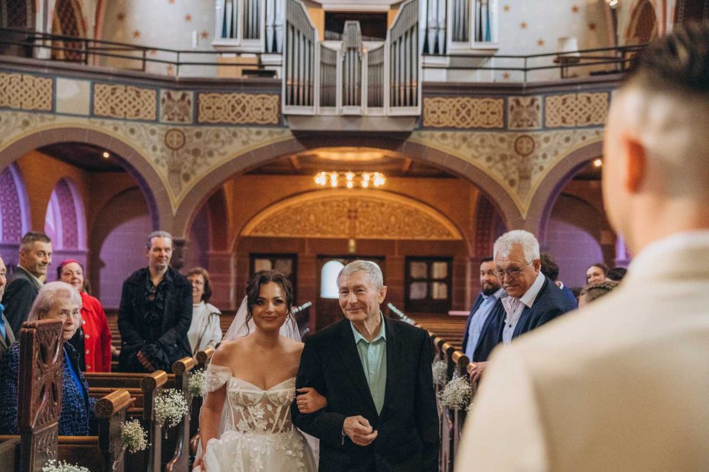 Brautpaar sitzt während der Trauung in der Kirche und blickt lächelnd über die Schulter, Hochzeit in Köln