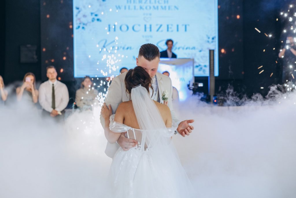 Brautpaar tanzt eng umschlungen im dichten Bodennebel vor der Willkommens-Leinwand beim ersten Tanz einer Hochzeit in Köln