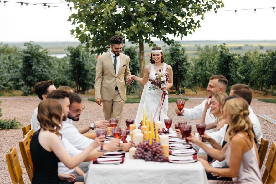Hochzeitsablauf im Freien: Brautpaar und Gäste an der festlich gedeckten Hochzeitstafel