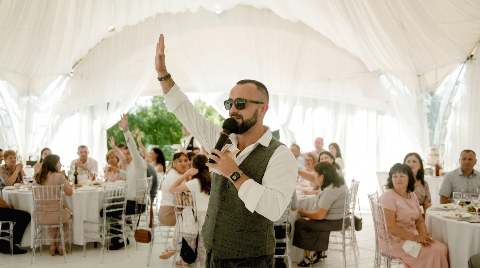 Hochzeitsmoderator Jens begeistert Gäste mit Mikrofon und erhobener Hand im Festzelt