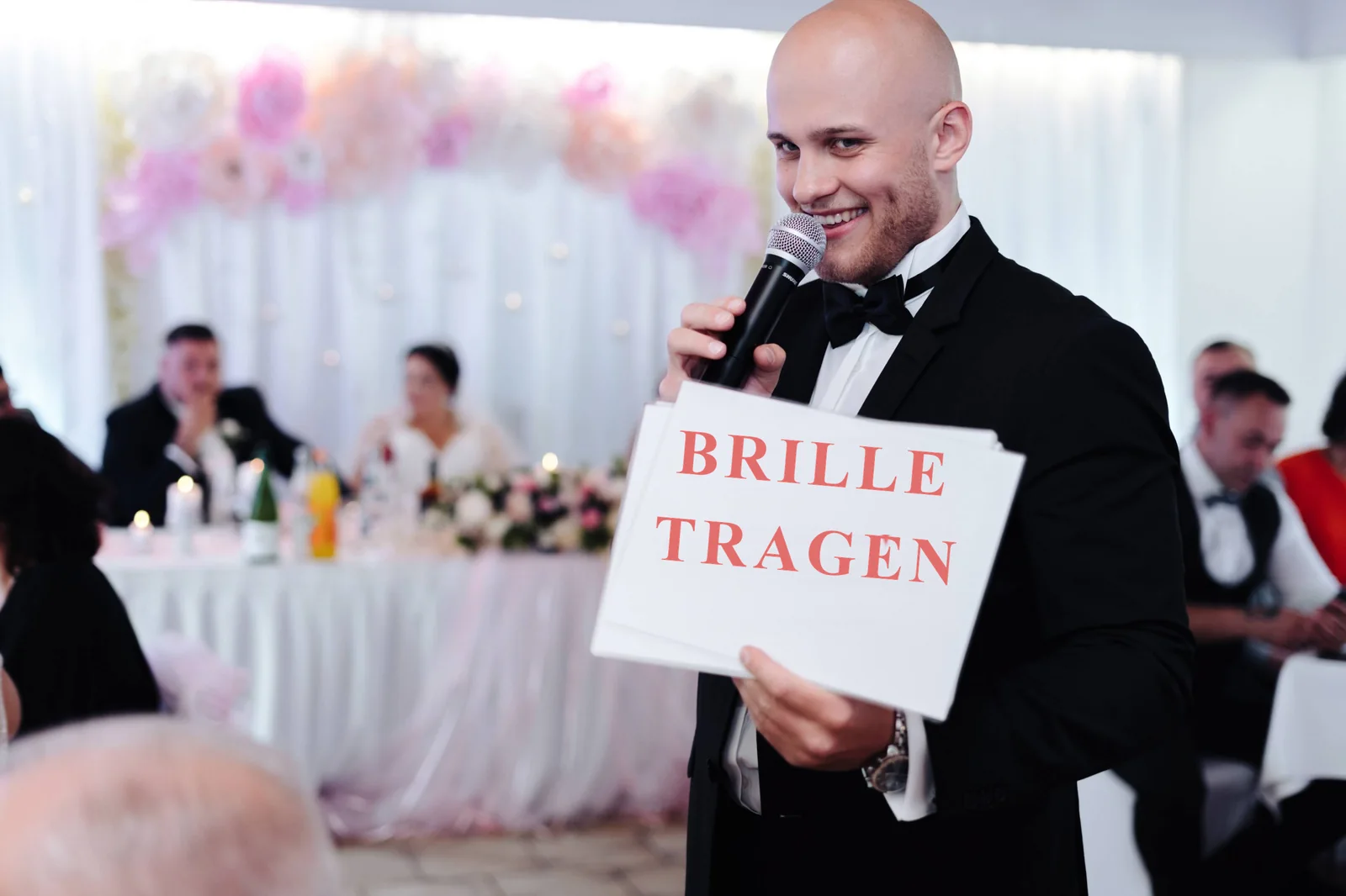 Moderator zeigt Gästen ein Schild mit der Aufschrift Brille tragen