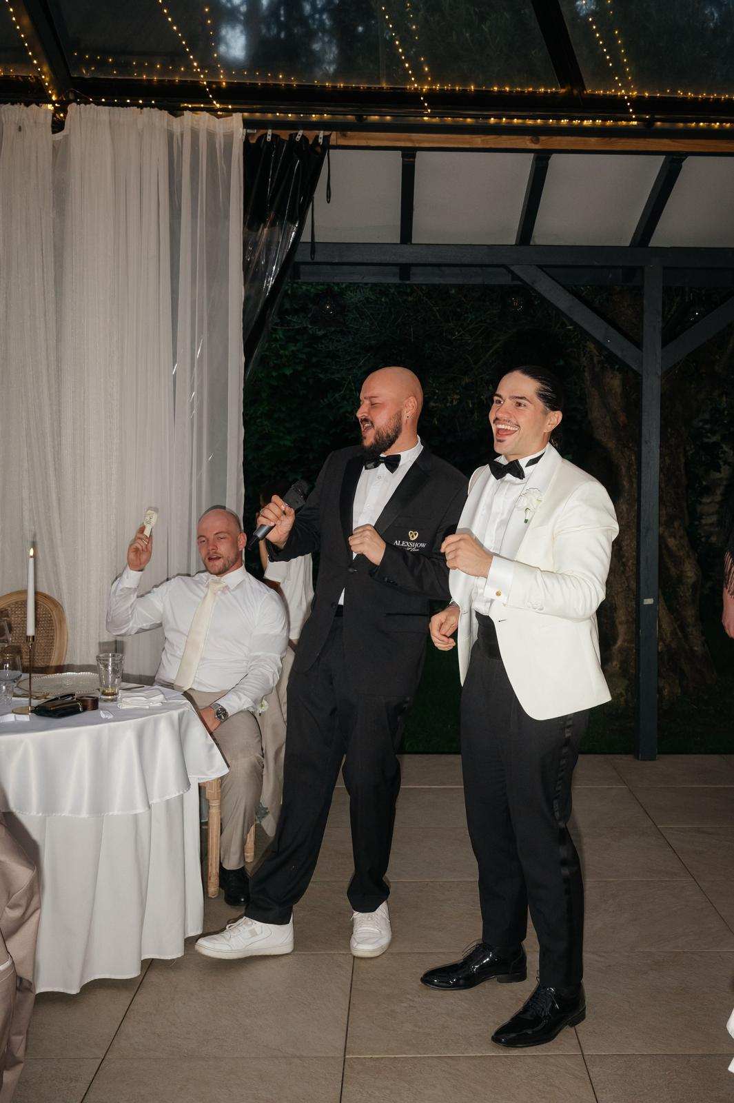 Hochzeitsmoderator Vincent mit Bräutigam bei der Hochzeitsfeier Hochzeitsmoderator Vincent mit Mikrofon neben dem lachenden Bräutigam bei der Hochzeitsfeier