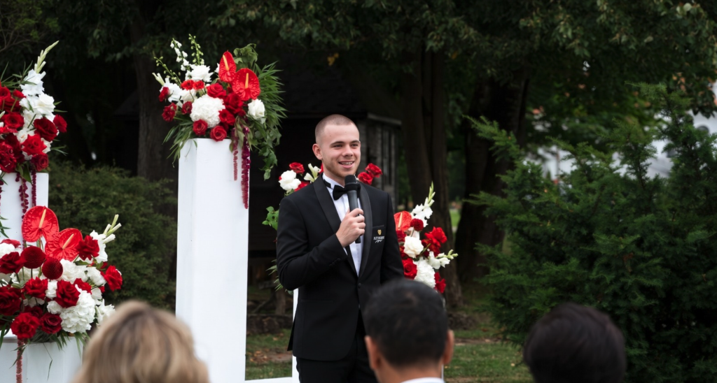 Luca mit Mikrofon bei einer Trauung zwischen roten und weißen Blumen