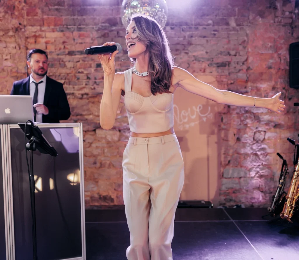 Natalie singt mit Mikrofon auf der Bühne, im Hintergrund ein DJ-Pult und eine Discokugel